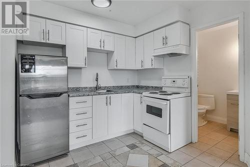 Kitchen with white electric stove, freestanding refrigerator, white cabinetry, under cabinet range hood, and light tile patterned floors - 897 Barton Street E, Hamilton, ON - Indoor Photo Showing Kitchen