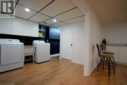Laundry room featuring a paneled ceiling, light wood finished floors, washing machine and clothes dryer, recessed lighting, and cabinet space - 