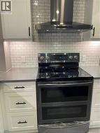 Kitchen with ventilation hood, stainless steel electric stove, white cabinetry, and decorative backsplash - 