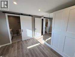 Unfurnished bedroom featuring a barn door, connected bathroom, light wood finished floors, a closet, and recessed lighting - 