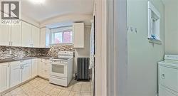 Kitchen with white range with electric stovetop, washer / clothes dryer, white cabinets, decorative backsplash, and light tile patterned floors - 