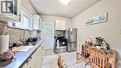 Kitchen featuring white cabinetry, appliances with stainless steel finishes, light tile patterned flooring, light countertops, and glass insert cabinets - 25 Spadina Avenue, Hamilton, ON - Indoor Photo Showing Kitchen