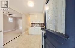 Kitchen with tasteful backsplash, white cabinets, light tile patterned floors, and electric range - 