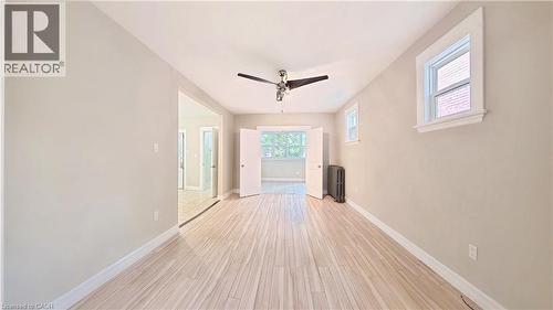 Empty room with a ceiling fan, light wood-style floors, and radiator - 25 Spadina Avenue, Hamilton, ON - Indoor Photo Showing Other Room