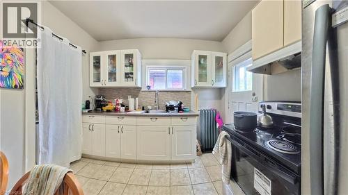 Kitchen with electric range, glass insert cabinets, stainless steel refrigerator, under cabinet range hood, and white cabinets - 25 Spadina Avenue, Hamilton, ON - Indoor Photo Showing Kitchen