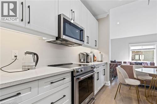 Kitchen with stainless steel appliances, white cabinets, light stone counters, ornamental molding, and light wood-style flooring - 24 Tamarack Way, Simcoe, ON - Indoor