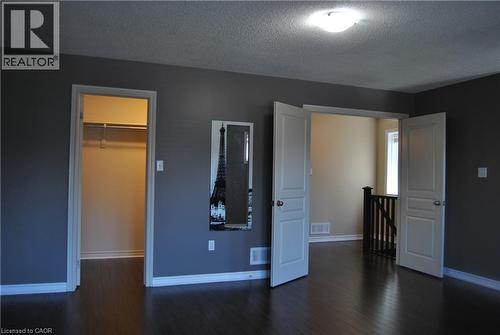 Unfurnished bedroom with a textured ceiling, a walk in closet, and dark wood-type flooring - 154 Harding Street, Kitchener, ON - Indoor Photo Showing Other Room