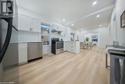 Kitchen with a peninsula, stainless steel appliances, white cabinets, light wood finished floors, and recessed lighting - 