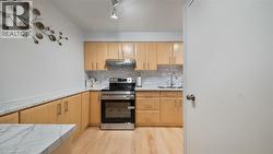 Kitchen featuring stainless steel electric range, light stone countertops, light brown cabinetry, decorative backsplash, and under cabinet range hood - 