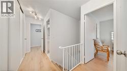 Hallway with an upstairs landing, a textured ceiling, and light wood-style floors - 