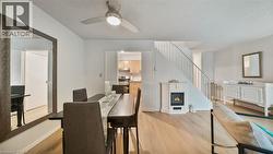 Dining space with light wood finished floors, a glass covered fireplace, a textured ceiling, stairway, and ceiling fan - 