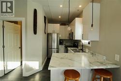 Kitchen with a kitchen bar, stainless steel appliances, hanging light fixtures, a peninsula, and white cabinets - 