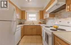 Kitchen with white appliances, under cabinet range hood, light countertops, light tile patterned floors, and decorative backsplash - 