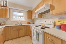 Kitchen featuring white electric range oven, under cabinet range hood, light brown cabinetry, light tile patterned flooring, and decorative backsplash - 