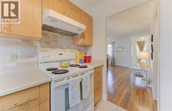 Kitchen featuring white electric range, under cabinet range hood, light brown cabinetry, backsplash, and light tile patterned flooring - 