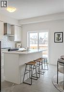 Kitchen featuring wall chimney range hood, a kitchen breakfast bar, backsplash, and white cabinets - 