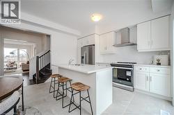 Kitchen with stainless steel appliances, wall chimney range hood, a kitchen breakfast bar, an island with sink, and white cabinets - 