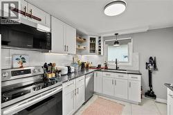 Kitchen featuring stainless steel appliances, decorative backsplash, decorative light fixtures, and white cabinetry - 