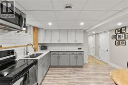 Kitchen featuring gray cabinetry, stainless steel appliances, light wood finished floors, white cabinets, and recessed lighting - 