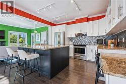 Kitchen featuring white cabinets, a kitchen breakfast bar, appliances with stainless steel finishes, light stone counters, and ornamental molding - 