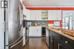 Kitchen with appliances with stainless steel finishes, white cabinetry, open shelves, light stone counters, and ornamental molding - 