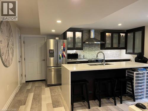 Kitchen featuring dark cabinetry, glass insert cabinets, stainless steel appliances, wall chimney range hood, and recessed lighting - 235 Fearnwood Street, Cambridge, ON - Indoor Photo Showing Kitchen