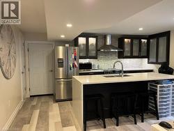 Kitchen featuring dark cabinetry, glass insert cabinets, stainless steel appliances, wall chimney range hood, and recessed lighting - 