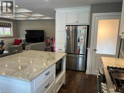 Kitchen with stainless steel appliances, white cabinets, open floor plan, coffered ceiling, and light stone countertops - 