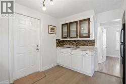 Kitchen with white cabinetry, freestanding refrigerator, glass insert cabinets, light wood finished floors, and backsplash - 