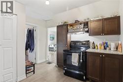 Kitchen featuring black range with electric stovetop, dark wood finish cabinetry, light countertops, open shelves, and light wood-type flooring - 