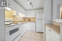 Kitchen with white appliances, under cabinet range hood, white cabinets, decorative backsplash, and light countertops - 