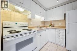 Kitchen with white appliances, under cabinet range hood, light countertops, white cabinets, and light tile patterned floors - 