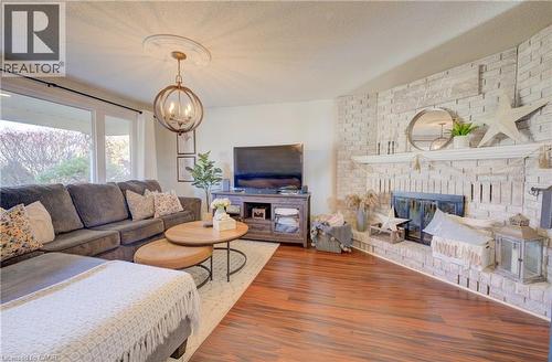 Great room with a brick fireplace, hardwood / wood-style floors, a textured ceiling, and an inviting chandelier - 47 Manor Drive, Kitchener, ON - Indoor Photo Showing Living Room With Fireplace