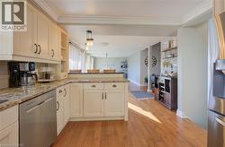 Kitchen with ornamental molding, appliances with stainless steel finishes, light stone countertops, kitchen peninsula, and light hardwood / wood-style flooring - 