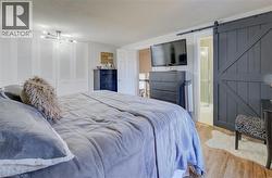 Bedroom with a textured ceiling, a barn door, connected bathroom, a closet, and light wood-type flooring - 