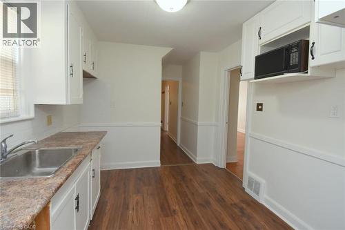 Kitchen featuring white cabinetry, dark wood finished floors, black microwave, light countertops, and tasteful backsplash - 136 Glen Road, Hamilton, ON - Indoor Photo Showing Kitchen