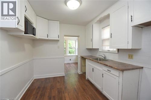 Kitchen with white cabinets, dark wood-style floors, dark countertops, black microwave, and backsplash - 136 Glen Road, Hamilton, ON - Indoor Photo Showing Kitchen