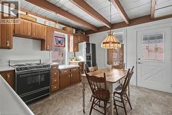 Kitchen with light countertops, black range with electric stovetop, brown cabinetry, pendant lighting, and beamed ceiling - 