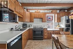 Kitchen with black appliances, light countertops, brown cabinetry, and beam ceiling - 