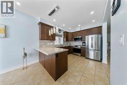 Kitchen with stainless steel appliances, dark wood finish cabinets, a peninsula, decorative light fixtures, and backsplash - 