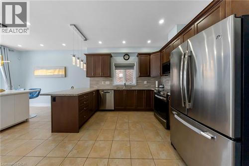 Kitchen featuring stainless steel appliances, a peninsula, dark wood finish cabinetry, pendant lighting, and light tile patterned flooring - 59 Greti Drive, Hamilton, ON - Indoor Photo Showing Kitchen