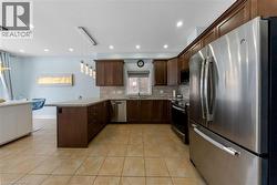 Kitchen featuring stainless steel appliances, a peninsula, dark wood finish cabinetry, pendant lighting, and light tile patterned flooring - 