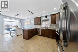 Kitchen with stainless steel appliances, dark wood finish cabinetry, a peninsula, pendant lighting, and light tile patterned flooring - 