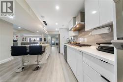 Kitchen with modern cabinets, white cabinetry, a breakfast bar, light wood-style floors, and a kitchen island with sink - 