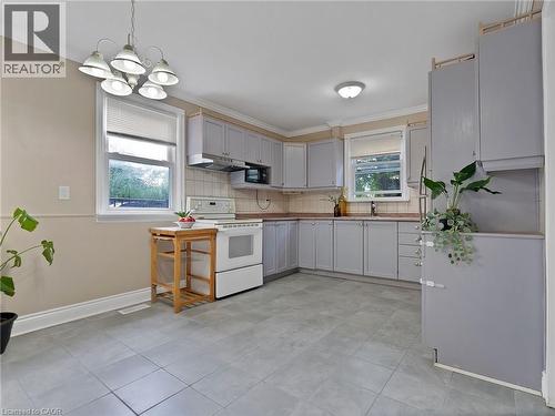 Kitchen with white electric stove, decorative light fixtures, ornamental molding, backsplash, and gray cabinetry - 210 East 24Th Street, Hamilton, ON - Indoor Photo Showing Kitchen
