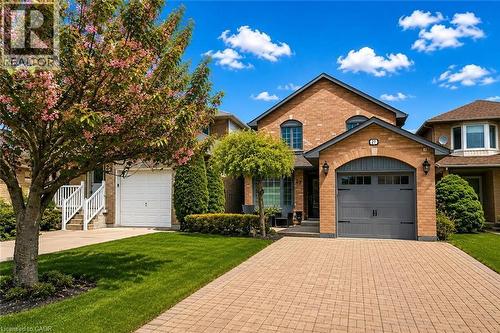 Brick exterior featuring a two-car garage with an arched stone facade, paver driveway, and manicured front lawn - 27 Beaverton Drive, Hamilton, ON - Outdoor With Facade