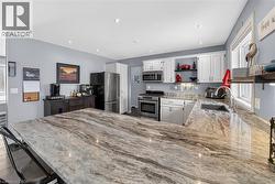 Kitchen featuring open shelves, light stone counters, white cabinets, stainless steel appliances, and a kitchen breakfast bar - 