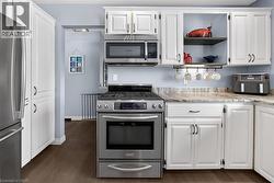 Kitchen with white cabinetry, stainless steel appliances, open shelves, and dark wood-style flooring - 