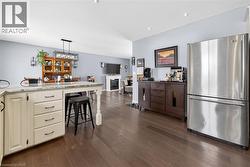 Kitchen featuring freestanding refrigerator, light stone counters, hanging light fixtures, dark wood finished floors, and a kitchen bar - 