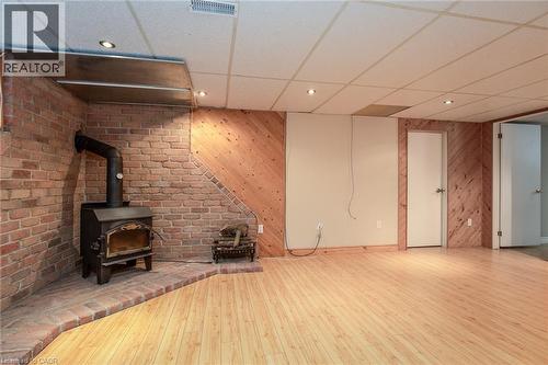 Unfurnished living room featuring wood walls, a drop ceiling, hardwood / wood-style floors, a wood stove, and brick wall - 120 Fourth Avenue, Kitchener, ON 